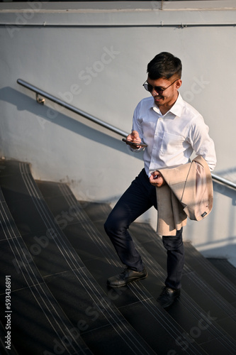 Confident Asian businessman chatting with someone on his phone while walking on the stairs in a city