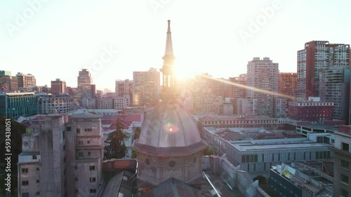 Aerial view orbiting Santiago Metropolitan Cathedral with glowing sunset passing behind the dome spire
