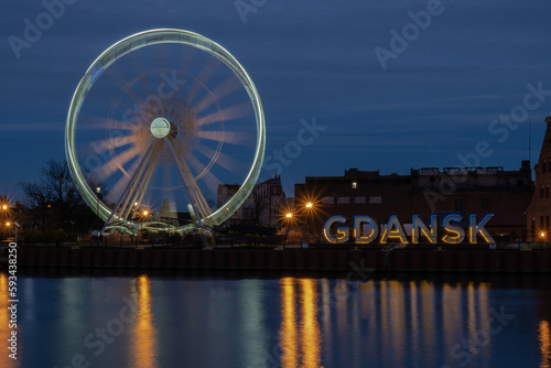 Gdansk Poland Ferris wheel in the old town of Gdansk at night evening dusk Reflection in river water Europe. Long exposure photo. City scenic view Illuminated attraction park and street with beautiful