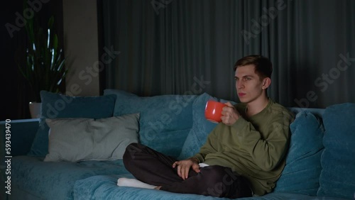 man watching TV alone while drinking tea. Man seems relaxed and comfortable in his own company, perhaps enjoying a quiet moment of leisure. personal relaxation, solitary entertainment.
