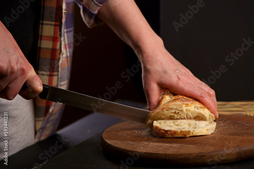 Whole grain bread put on kitchen wood plate with a chef holding knife for cut. The healthy eating and traditional bakery concept. Front viev. Fresh bread on table close-up