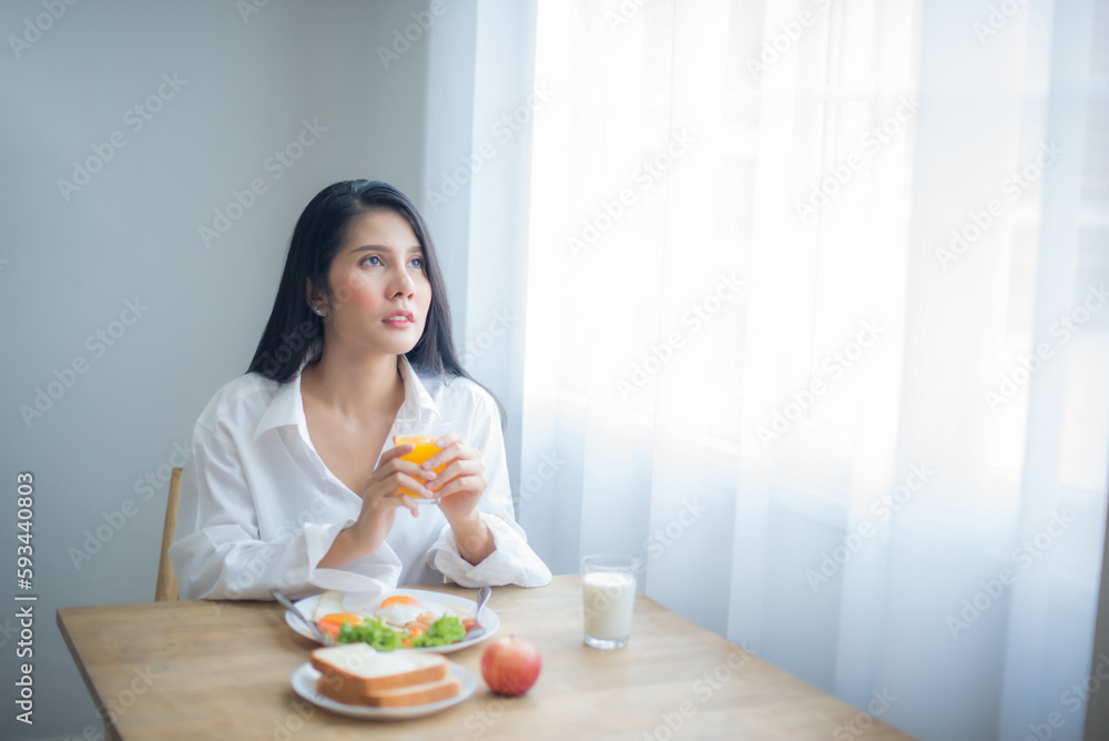 Beautiful asian woman hold the glass of juice in one hand and looked to the copy space with a serene expression on her face.