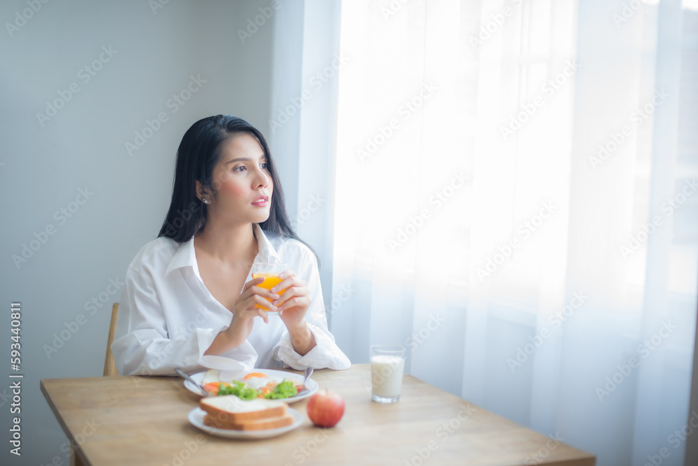 Beautiful asian woman holding glass of juice while looking to the copy space with breakfast on the table. Beautiful asian woman holding glass of juice while looking to the copy space with breakfast on the table.
