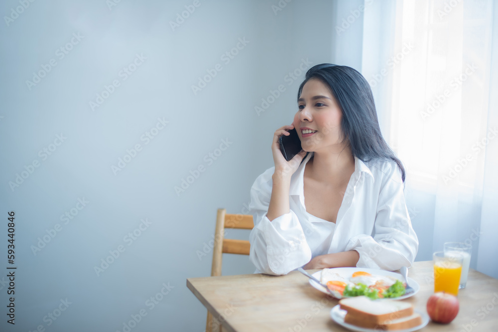 Beautiful asian girl talking on the phone with a happy expression before having a nutritious breakfast. Beautiful asian girl talking on the phone with a happy expression before having a nutritious breakfast.