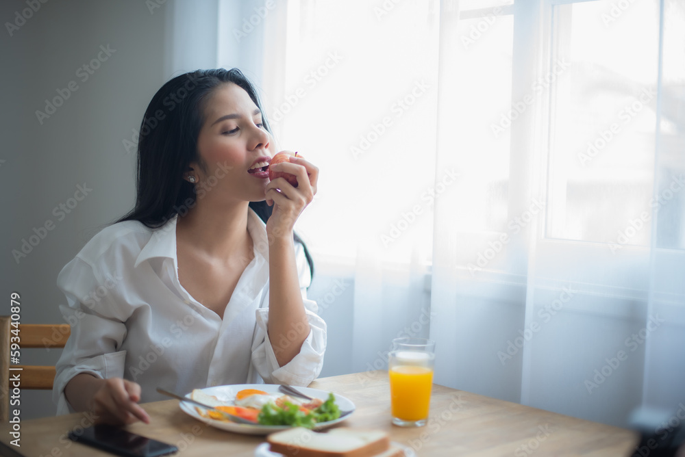 Beautiful asian woman eating an apple and on the table having breakfast and a glass of juice.