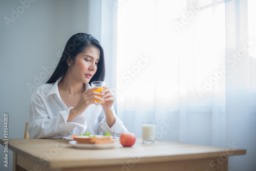 Beautiful asian woman's eyes were fixated on the copy space, and she hold the glass of juice with a steady hand.