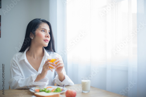 Beautiful asian woman gazed wistfully at the copy space as if lost in thought holding the glass of juice with a delicate grip.