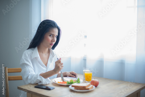 Beautiful asian girl looking at the camera with a disappointed look at her breakfast.