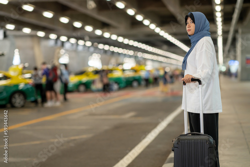 An Asian Muslim wearing a blue hijab is preparing for a vacation and she is at the airport. She's going to call a taxi, Muslim travelers. © maya1313