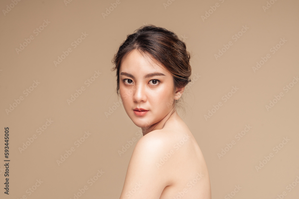 Beautiful asian woman in natural look makeup and showing perfect skin on her shoulder in isolated beige background. Beautiful asian woman in natural look makeup and showing perfect skin on her shoulder in isolated beige background.