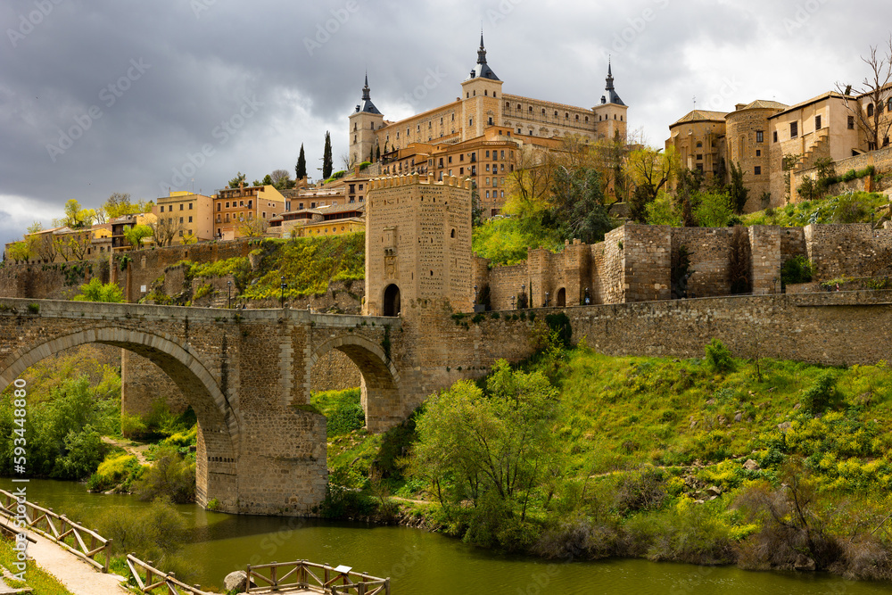 Scenic spring cityscape of old town of Toledo with Alcantara bridge and Alcazar fortress, central Spain