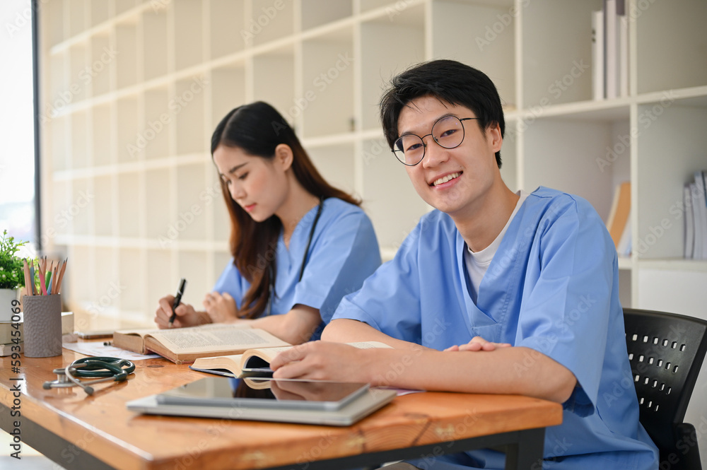 Handsome and smart young Asian male medical student in a uniform studying with his friend Handsome and smart young Asian male medical student in a uniform studying with his friend