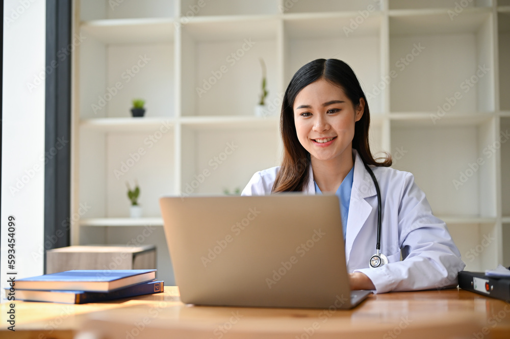 An Asian female doctor in a uniform using her laptop at her desk in her office. An Asian female doctor in a uniform using her laptop at her desk in her office.