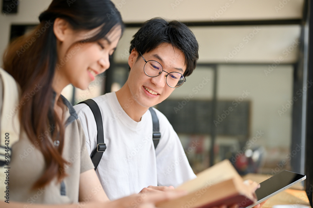 Happy Asian male college student tutoring history to his girlfriend at a cafe on the weekend. Happy Asian male college student tutoring history to his girlfriend at a cafe on the weekend.