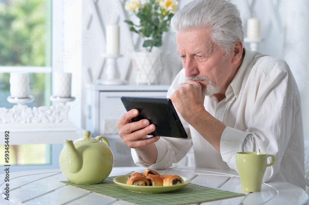 senior man using tablet while drinking tea senior man using tablet while drinking tea