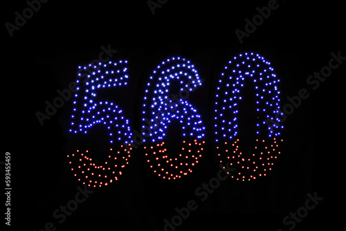 Drone light shows on black night sky background. A figure of the number five hundred and sixty, six, five, zerro, 560 made of glowing drones. photo