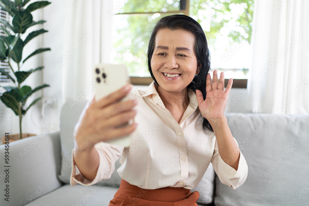 Middle age Asian woman holding cell telephone Work from home. smiling Beautiful mature asian woman VDO Call Conference smart phone with technology concept Middle age Asian woman holding cell telephone Work from home. smiling Beautiful mature asian woman VDO Call Conference smart phone with technology concept