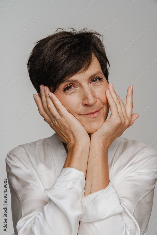 Senior woman touching her face and smiling at camera while standing isolated over white background Senior woman touching her face and smiling at camera while standing isolated over white background