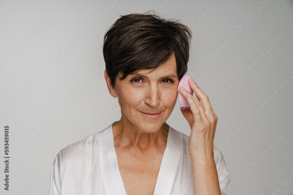 Senior woman using face cleansing brush isolated over white background Senior woman using face cleansing brush isolated over white background