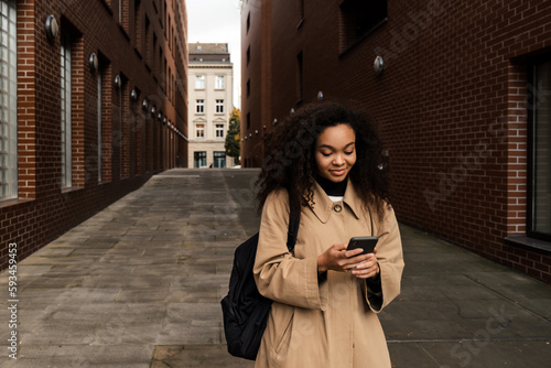 Beautiful african girl using smartphone while standing outdoors © Drobot Dean