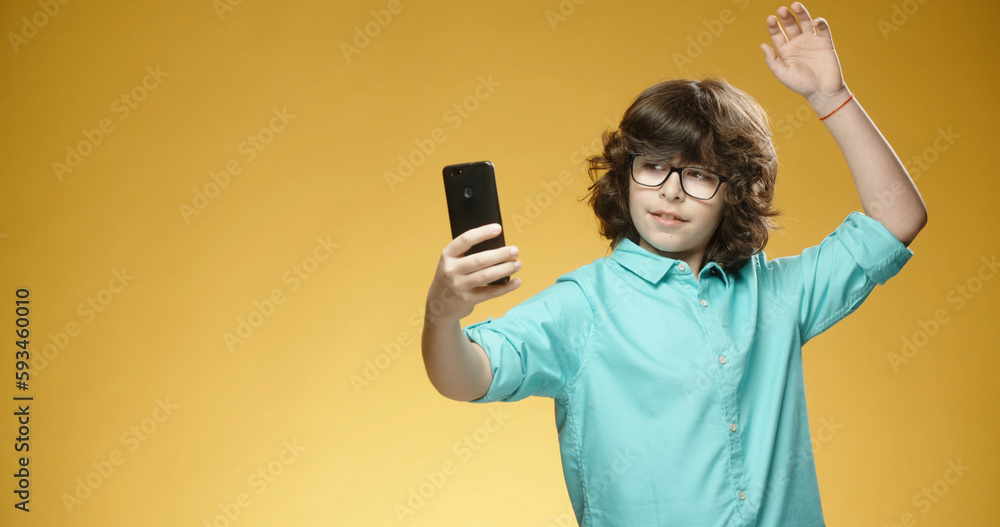 Cute little boy using his mobile phone to take pictures or selfies and positively smiling, isolated on yellow background - always online, emotions concept close up Cute little boy using his mobile phone to take pictures or selfies and positively smiling, isolated on yellow background - always online, emotions concept close up