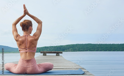 back view mature woman in pink sportswear practices yoga on a wooden deck near the sea.