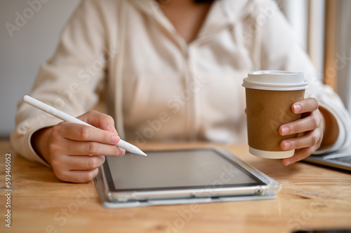 Close-up image of an Asian woman drawing artwork on her digital tablet in a coffee shop.