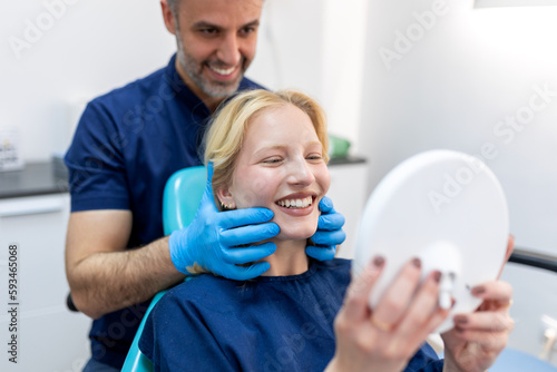 European young woman smiling while looking at mirror in dental clinic. Shot of a young woman checking her results in the dentists office