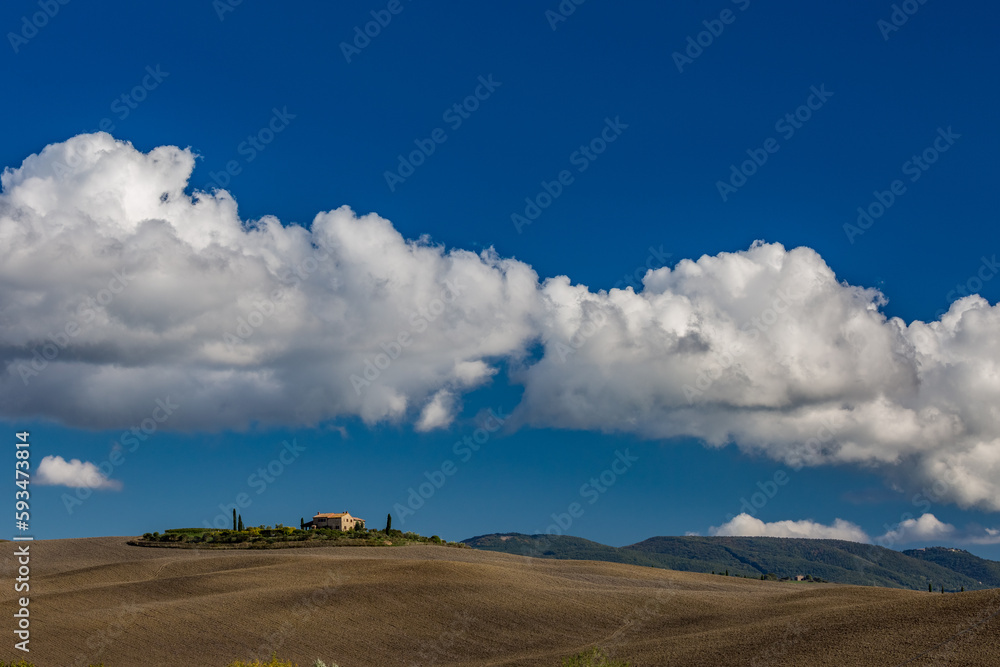 Plowed autumn field with house on the hill and layer of clouds in the bright blue sky over Tuscany countryside, Italy