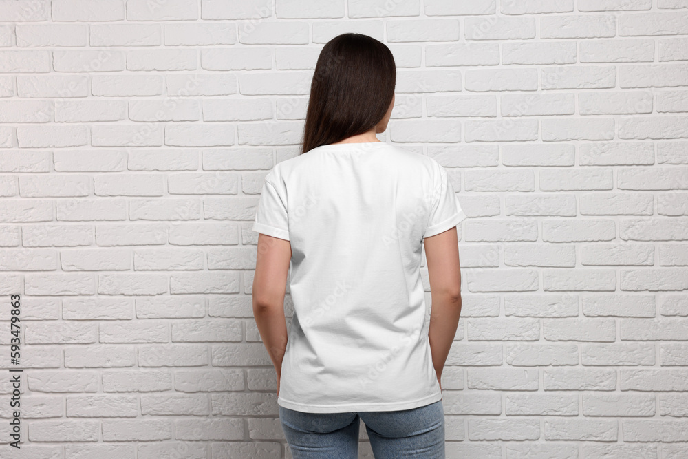 Woman wearing stylish T-shirt near white brick wall, back view Woman wearing stylish T-shirt near white brick wall, back view