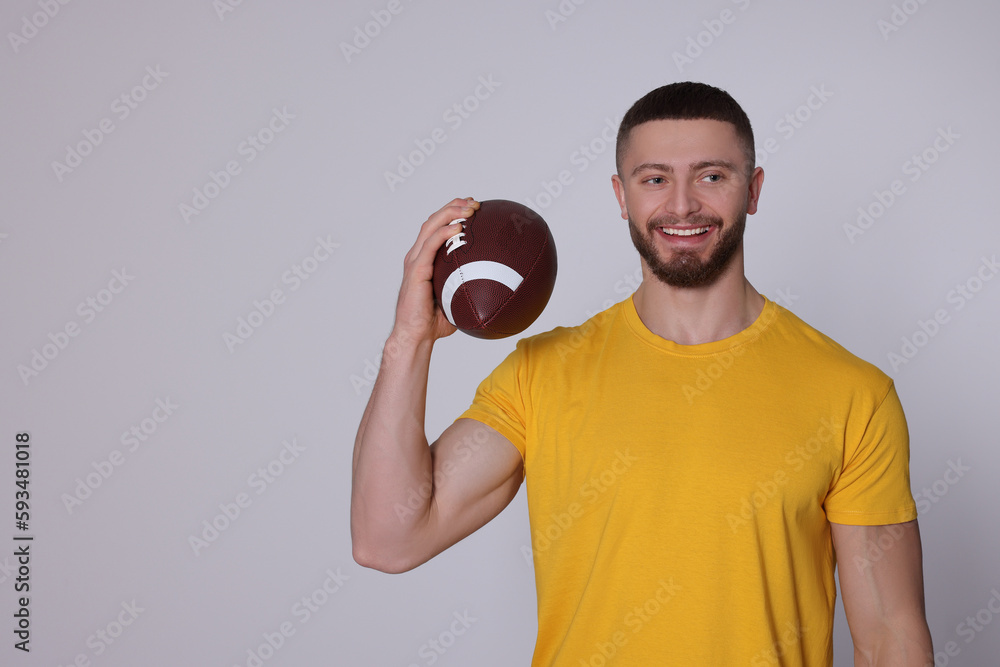Athletic young man with American football ball on light grey background. Space for text Athletic young man with American football ball on light grey background. Space for text