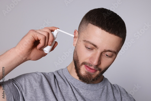 Man using ear spray on light grey background