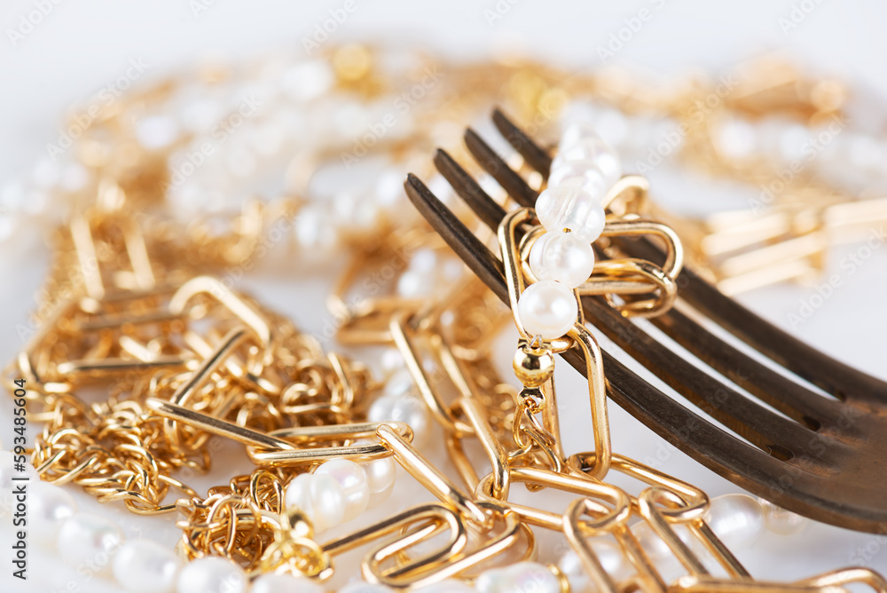 Jewelry bijouterie gold chain and pearl necklace on a fork, close-up. Shopaholism, waste of money, luxury concept. Jewelry bijouterie gold chain and pearl necklace on a fork, close-up. Shopaholism, waste of money, luxury concept.