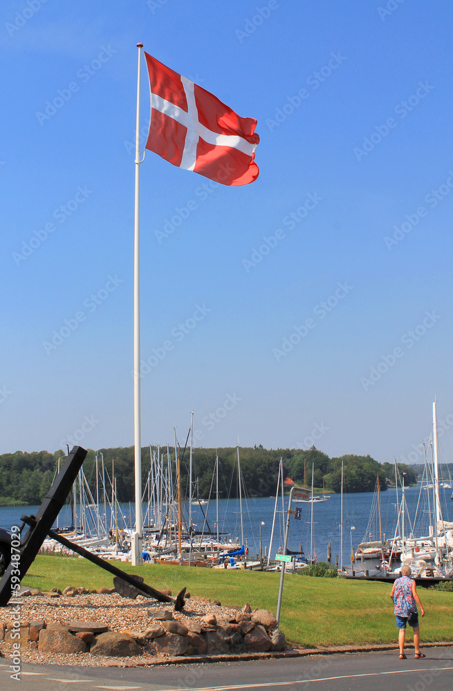 Danish flag by a pier with sailboats on a sunny summer day with a blue sky in Denmark
