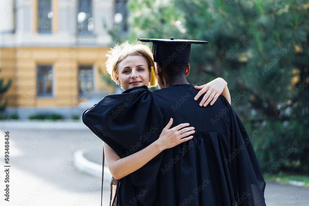 Black student in graduation mantle and hat gratefully hugging with ...