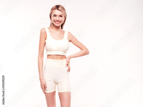 Young beautiful smiling blond female in trendy summer cycling shorts clothes. Sexy carefree woman posing on white background in studio. Positive model having fun indoors. Cheerful and happy. Very slim