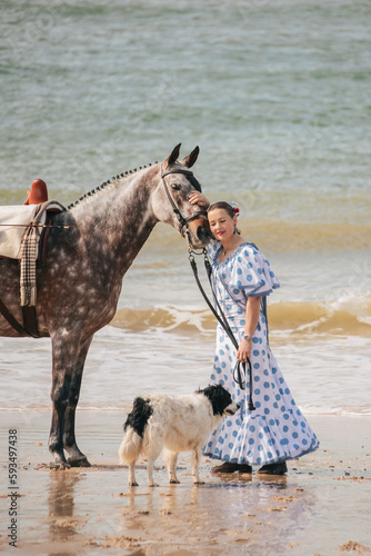 Woman in flamenco dots dress hugging horse on the beach