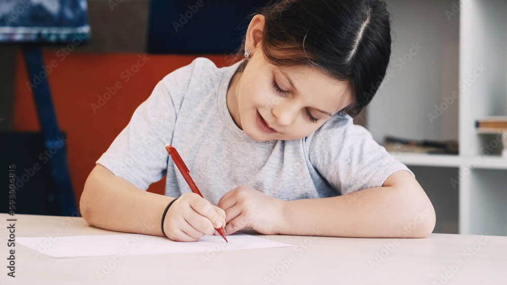 Kids painting. Art hobby. Creative time. Happy girl drawing with pencil on paper sitting table in light room interior. Kids painting. Art hobby. Creative time. Happy girl drawing with pencil on paper sitting table in light room interior.