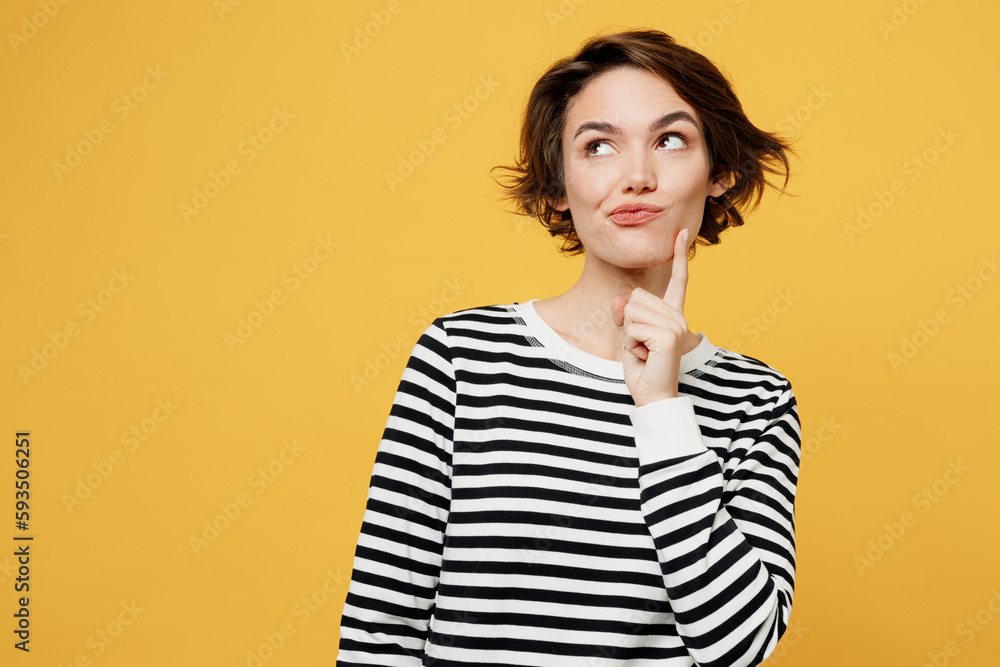Young minded fun woman wear casual striped black and white shirt put hand prop up on chin, lost in thought and conjectures isolated on plain yellow color background studio portrait. Lifestyle concept. Young minded fun woman wear casual striped black and white shirt put hand prop up on chin, lost in thought and conjectures isolated on plain yellow color background studio portrait. Lifestyle concept.