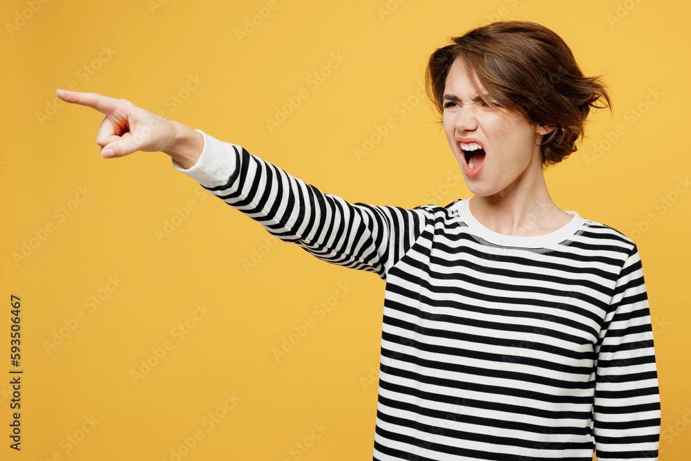 Young angry mad dissatisfied displeased sad woman wear casual striped black and white shirt point index finger aside scream isolated on plain yellow color background studio portrait Lifestyle concept Young angry mad dissatisfied displeased sad woman wear casual striped black and white shirt point index finger aside scream isolated on plain yellow color background studio portrait Lifestyle concept
