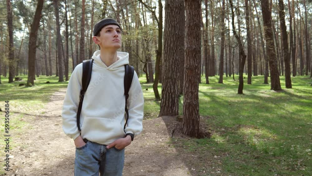 A young man in a white jacket and a hat with a backpack walks in the forest. Slow motion portrait A young man in a white jacket and a hat with a backpack walks in the forest. Slow motion portrait