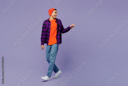 Full body young man of African American ethnicity wears casual shirt orange hat point index finger back aside indicate on workspace area copy space mock up isolated on plain purple color background.