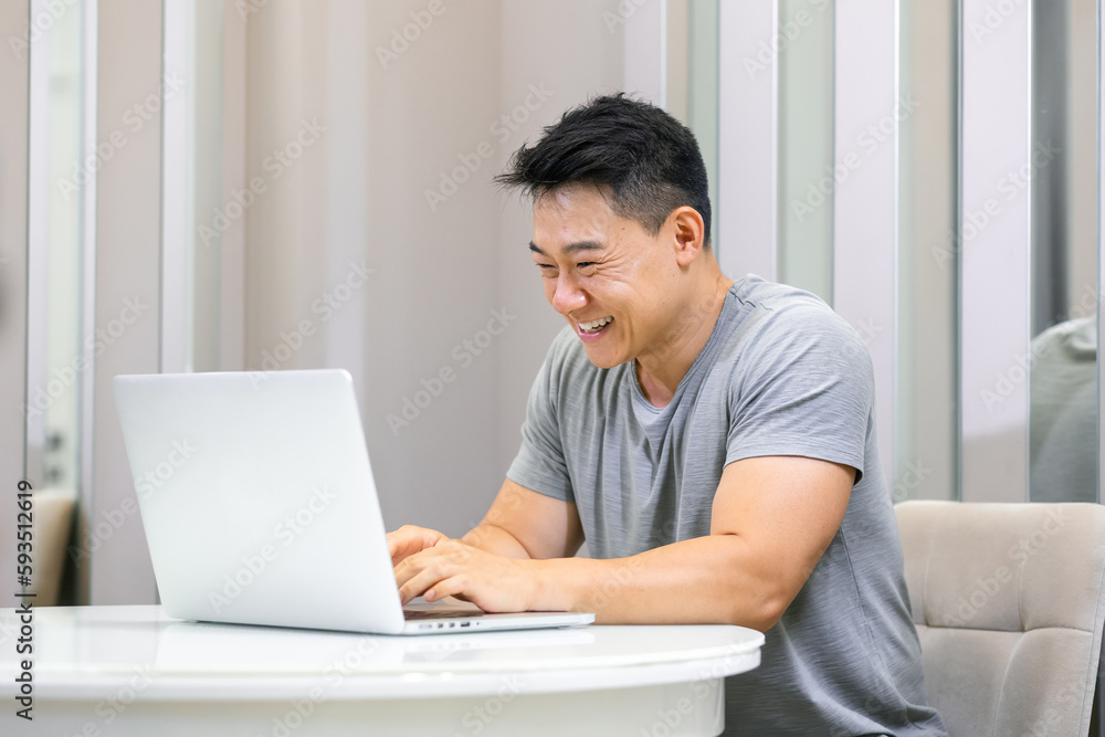 Portrait of young smiling asian man using pc sitting at desk, typing on keyboard. Cheerful guy browsing internet, surfing web. Portrait of young smiling asian man using pc sitting at desk, typing on keyboard. Cheerful guy browsing internet, surfing web.