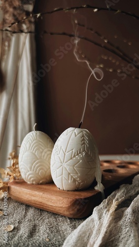 Traditional Easter decor.Burning soy candles in the shape of white eggs on a brown background