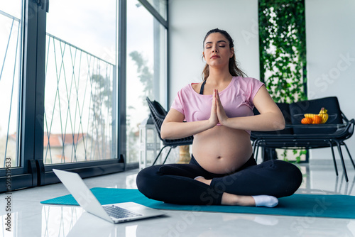 sporty pregnant woman sit on mat meditate practice yoga with online class on computer at home.