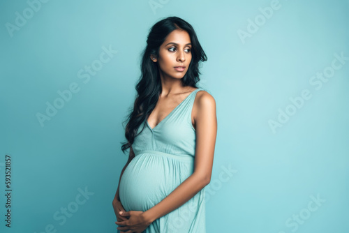 Expecting Joy: Pregnant Indian woman with hands on belly on pastel blue background with space for text. Copy space. Pregnancy and Maternity concept - AI Generative