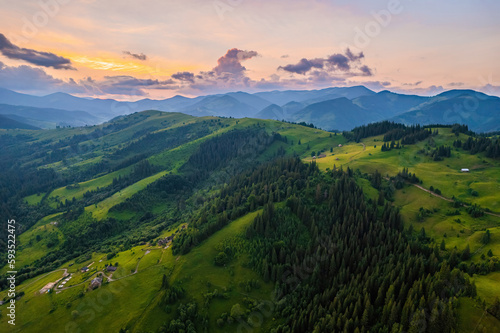 Mountains in clouds at sunrise in summer. Aerial view of mountain peak with green trees in fog. Beautiful landscape with high rocks  forest  sky.