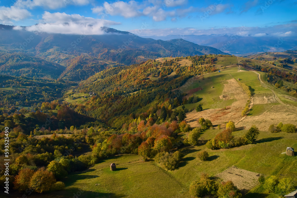 Fototapeta premium Aerial view of mountains at sunrise in autumn in Ukraine. Colorful landscape with mountain road, forest, houses on the hills, sunlight, sky in fall.