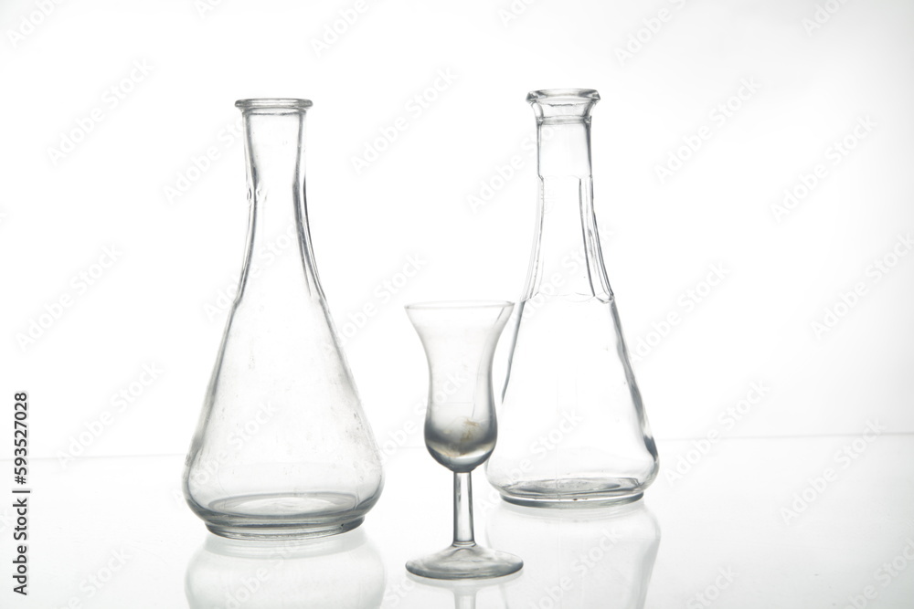 Transparent glass bottles and a small glass goblet isolated on the empty white background Transparent glass bottles and a small glass goblet isolated on the empty white background