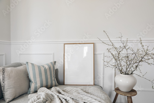 Spring home decor. Elegant scandinavian living room interior. Wooden picture frame, poster mockup on sofa. Linen striped cushions, throw. Blurred background. Cherry plum blossoms in vase, wooden stool